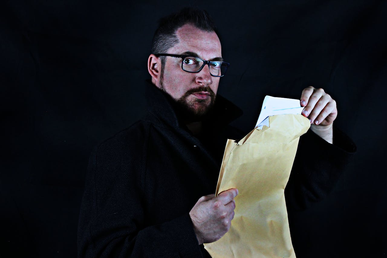 Services-03 Portrait of a man with eyeglasses opening a brown envelope, dark background.